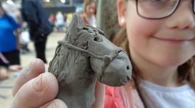 a young girl showing off the horses head she has made on a clay modelling experience day