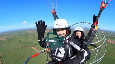 man smiling and waving while in the air on a paramotoring experience