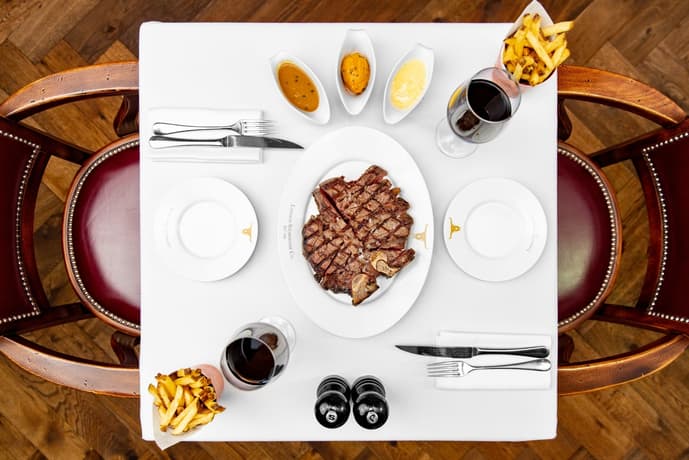 a view from above of a restaurant table laid out with a plate of steak in the middle, fries and sauces on the side