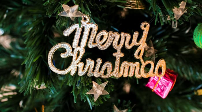 A christmas decoration spelling out merry christmas hanging on a christmas tree