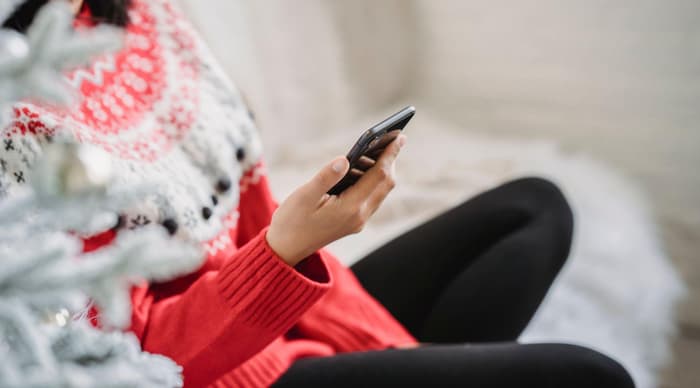 A woman curled up on the sofa looking at her phone with mug in hand christmas lights around her