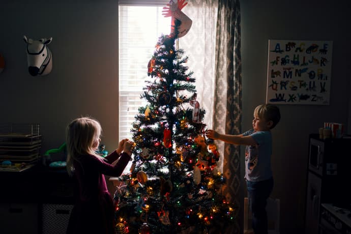 Children hanging decorations on a christmas tree outside at night
