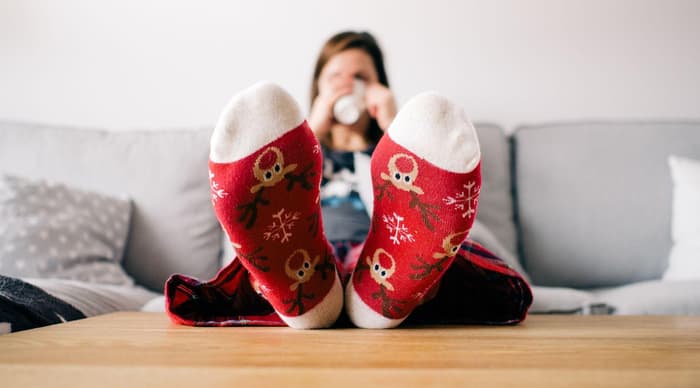Feet in red and white stripy socks in front of a fireplace with a christmas cookie and mug