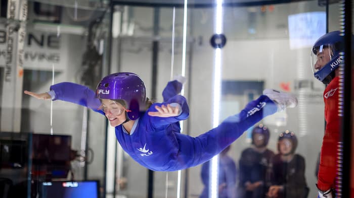 a young girl wearing a blue flight suit, goggles and helmet on an indoor skydiving experience