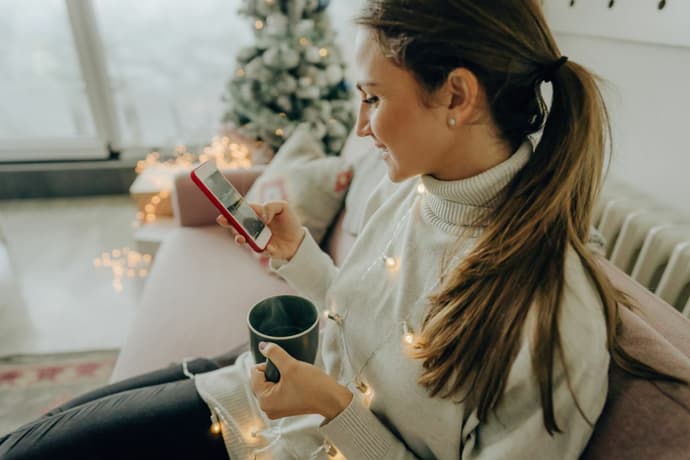 Lady sat on a sofa with her phone in one hand and a cup of tea in the other