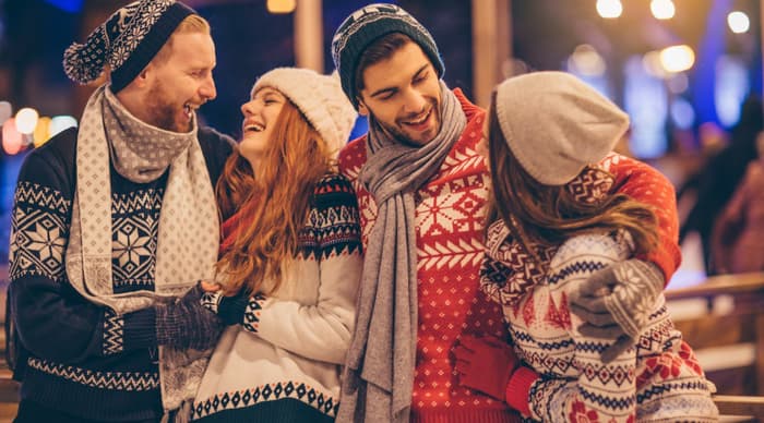 Two couples wearing christmas jumpers hats and scarves and laughing