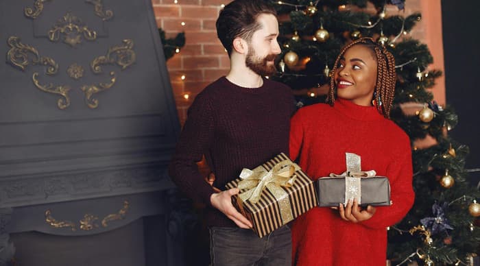 Woman opening christmas gift with man covering her eyes to surprise her