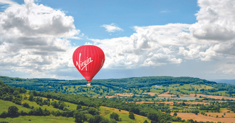 red virgin hot air balloon floating over countryside
