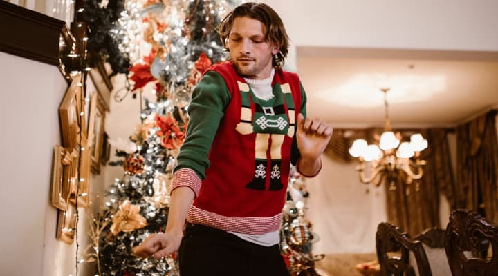 Man dancing wearing a christmas jumper infront of a christmas tree