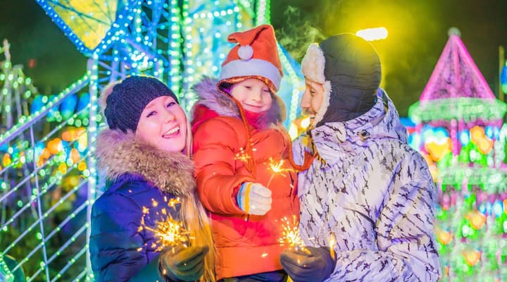 Mum dad and young daughter with sparklers in front of christmas tree