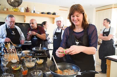 people being taught a cookery lesson in a kitchen with the help of professional chefs on a cookery course experience day