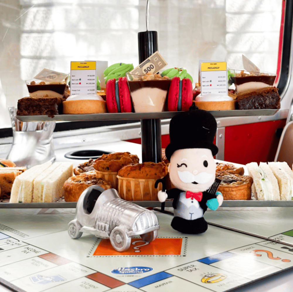 a selection of cakes and sandwiches on a monopoly board on an afternoon tea bus tour