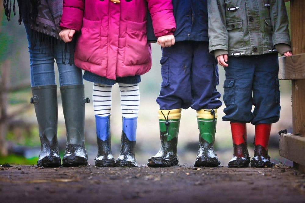 four children in a row all dressed for a walk outside and wearing wellington boots