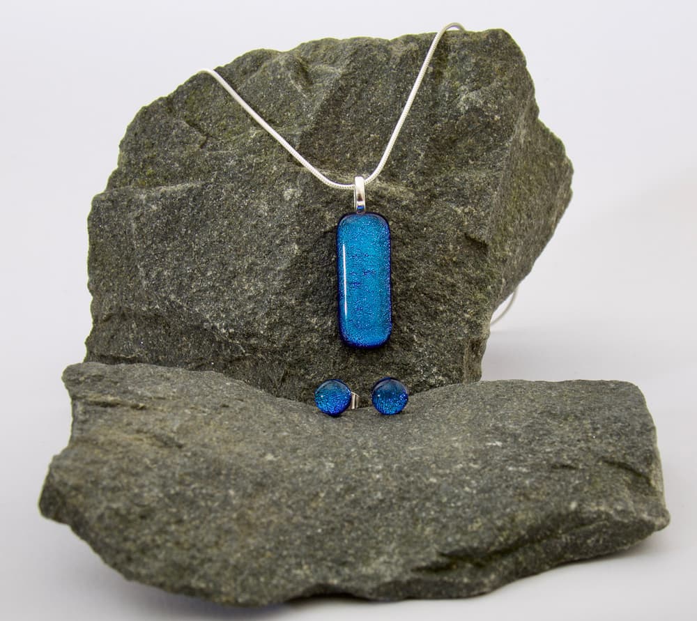 a jewellery set of necklace and earrings made from blue glass resting on a stone background
