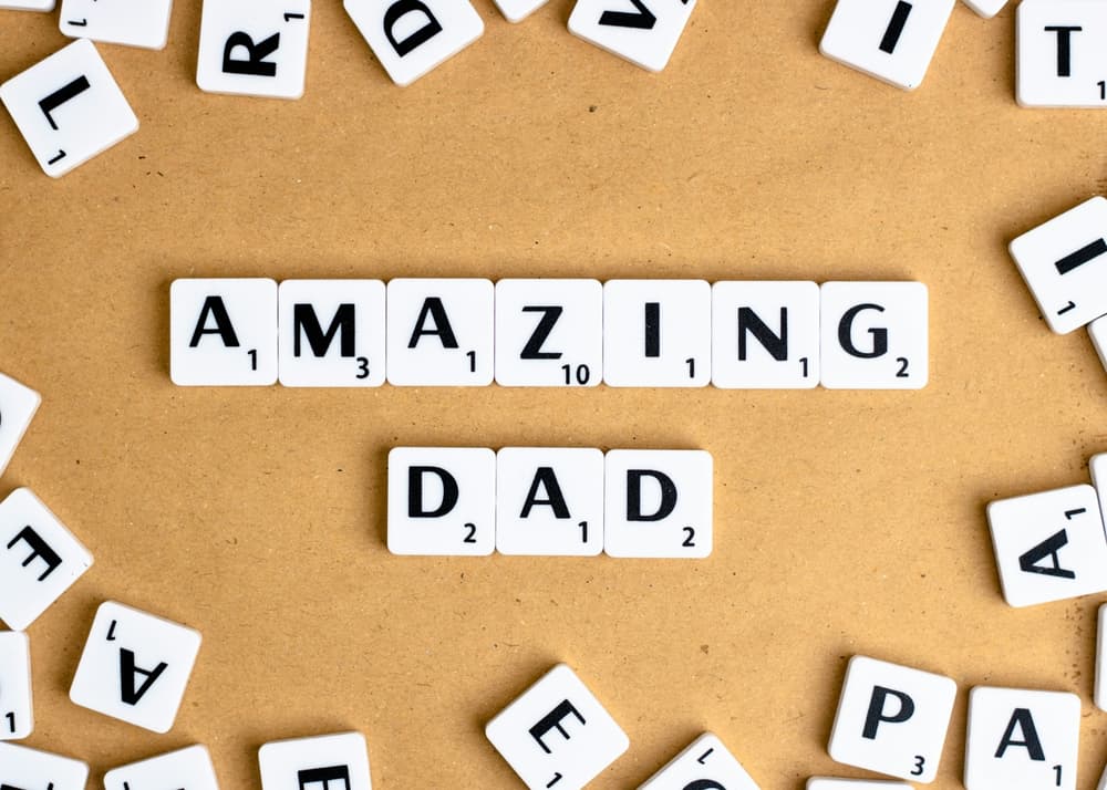 white scrabble letters laid out on a wooden board spelling out amazing dad