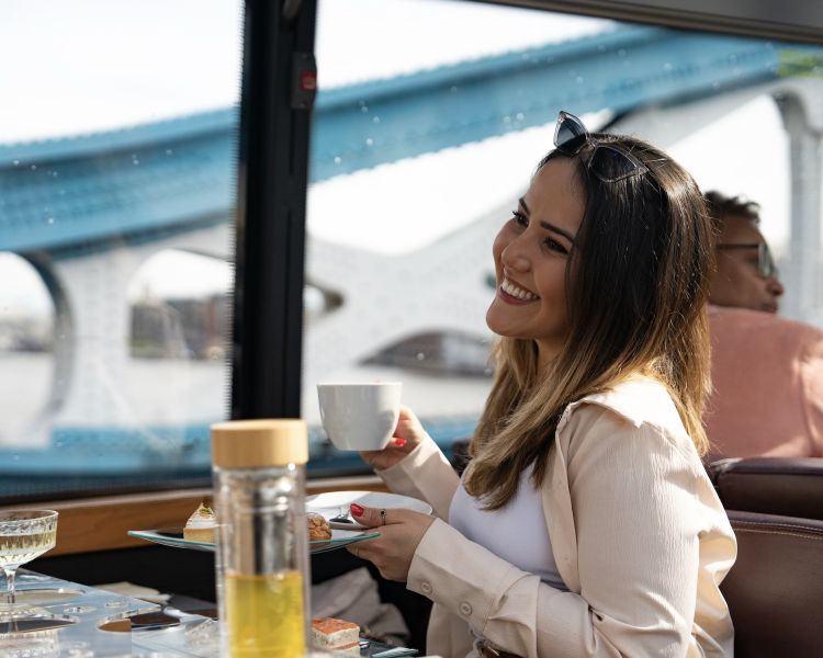 woman smiling drinking tea while having afternoon tea on bustronome london