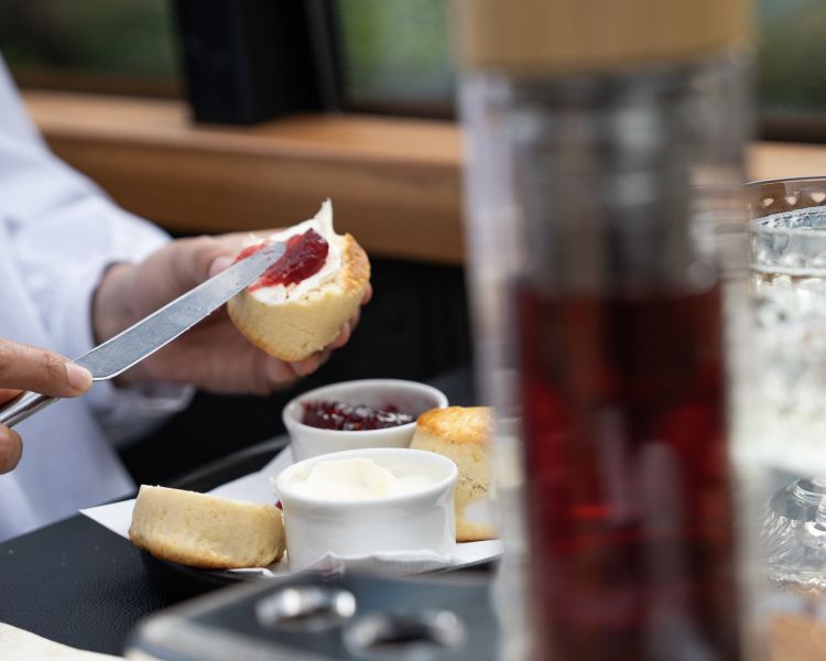 man spreading jam on scone at afternoon tea on bustronome london bus
