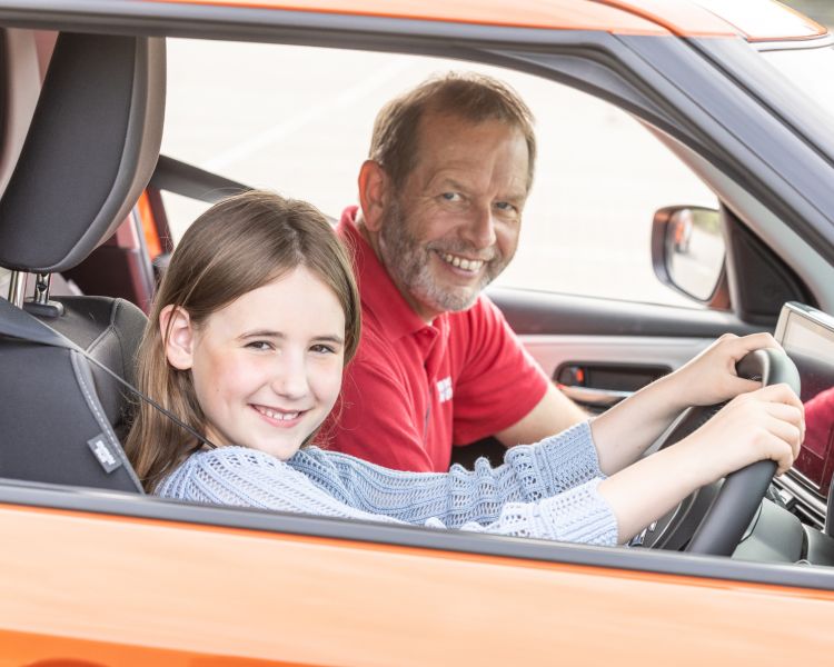 A young driver and instructor smiling in an orange car