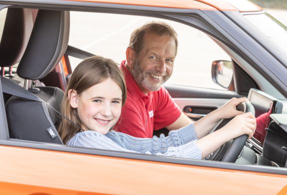 A young driver and instructor smiling in an orange car