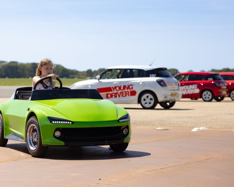A young girl driving a green firefly car