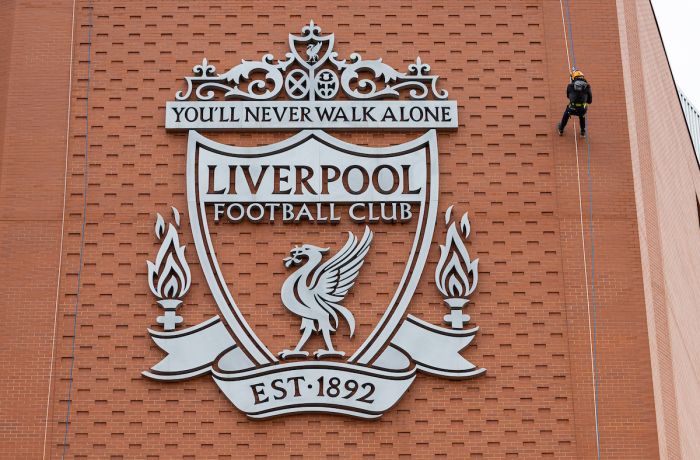 person abseiling down the side of anfield stadium next to the liverpool fc crest