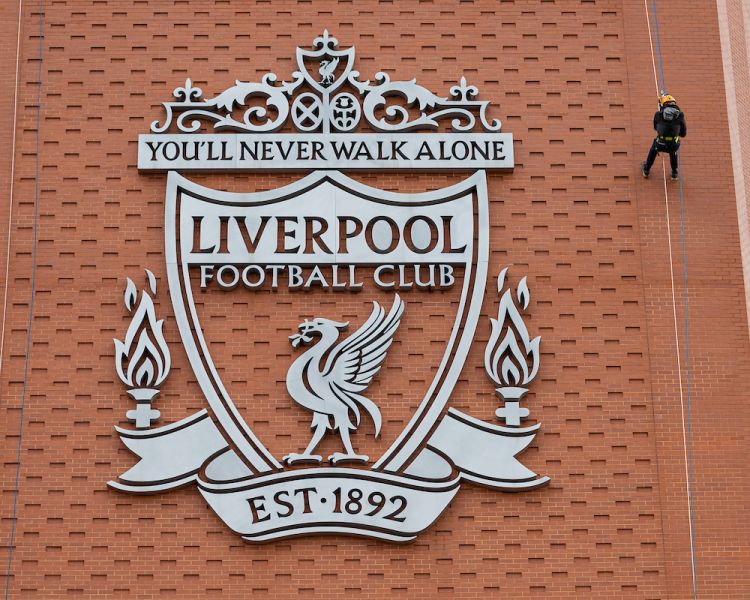 person abseiling down the side of anfield stadium next to the liverpool fc crest