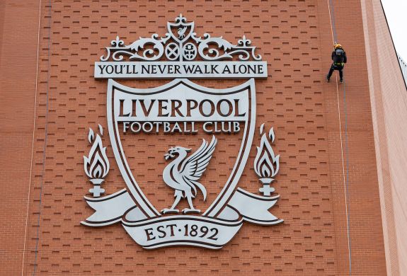 person abseiling down the side of anfield stadium next to the liverpool fc crest
