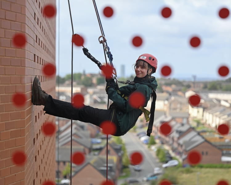 woman abseiling down the side of anfield stadium in liverpool seen through a window with red spots on