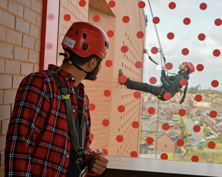 man looking through a window with red spots on at a woman abseiling down the side of anfield stadium
