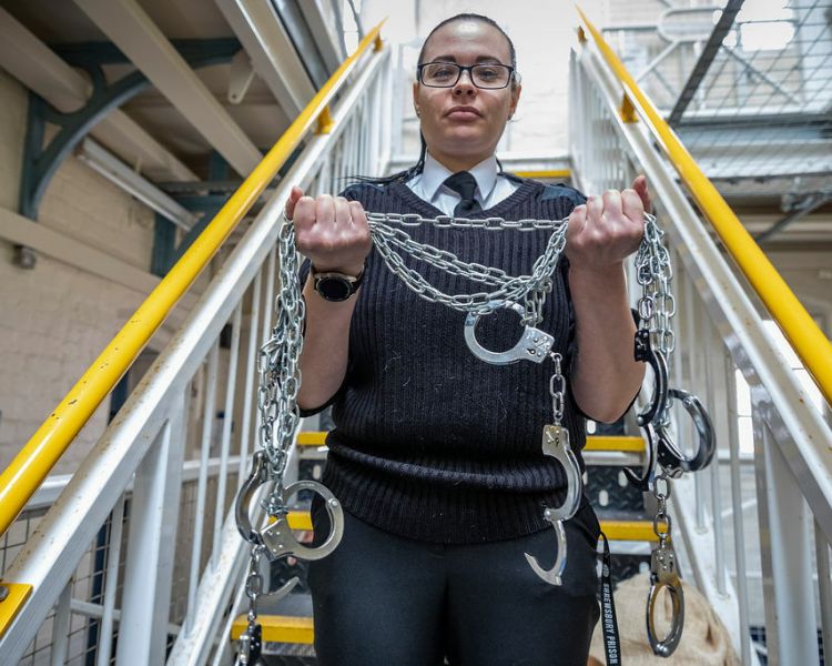 a woman prison guard holding multiple chains and handcuffs on a prison escape room experience day