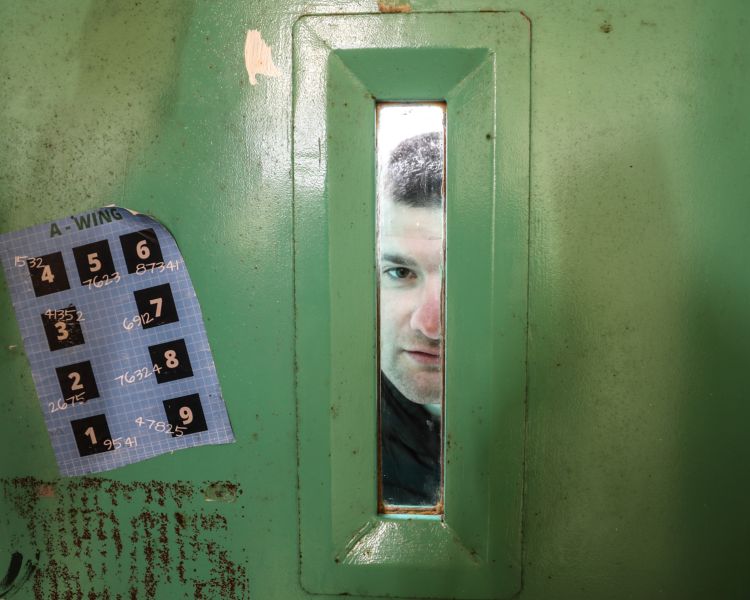 man looking through a small window on a cell door on a prison escape room experience day