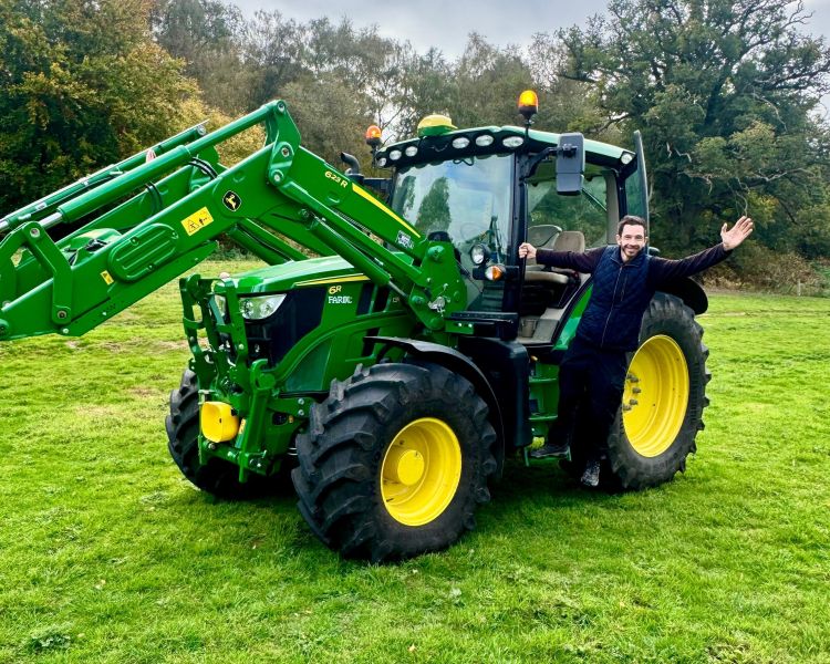 man posing for photo hanging on to the side of a tractor on a tractor driving experience