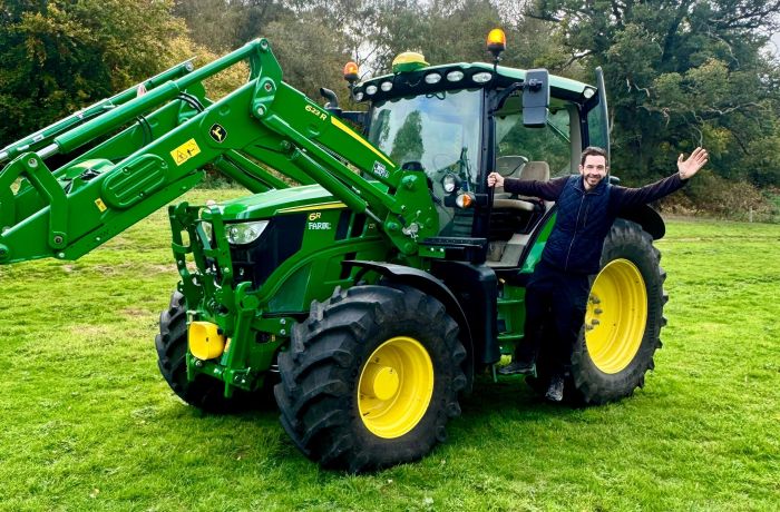 man posing for photo hanging on to the side of a tractor on a tractor driving experience