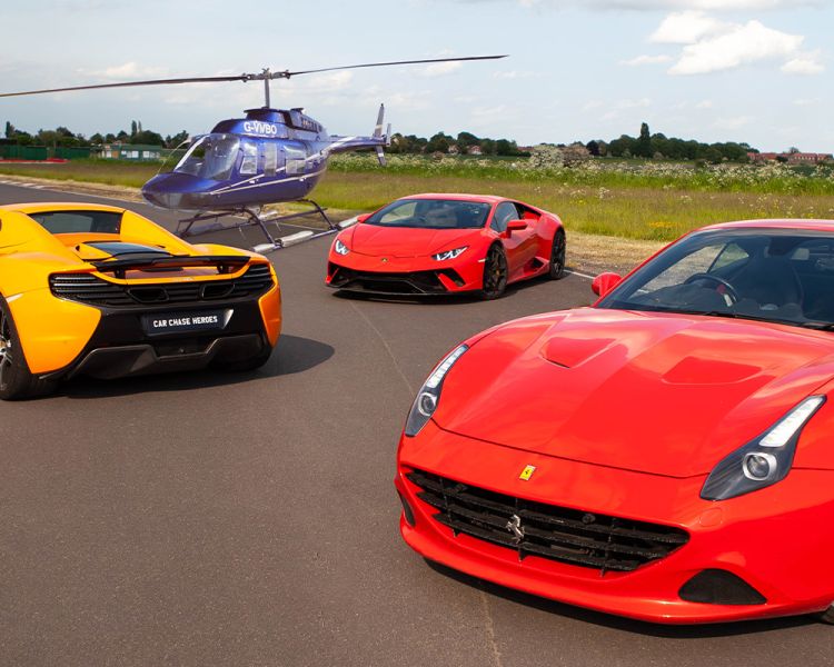 three supercars on a track with a helicopter in the background