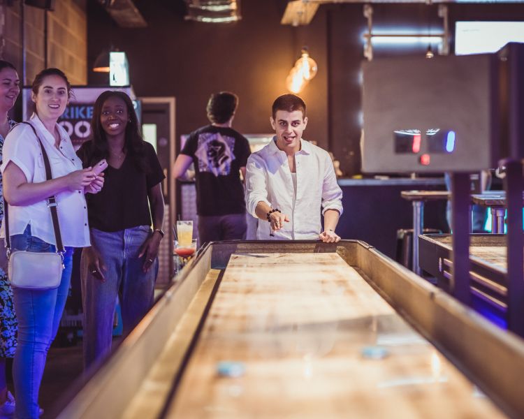 friends playing shuffleboard at a boom battle bar