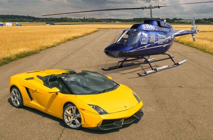 a yellow supercar on a track with a blue helicopter behind it