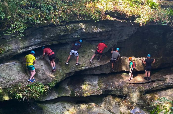 people walking and climbing along the edge of a gorge overlooking a river