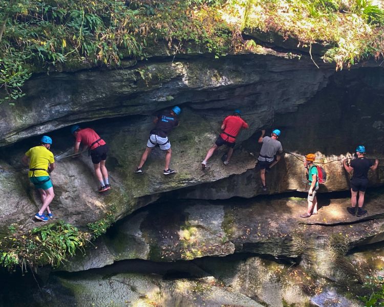 people walking and climbing along the edge of a gorge overlooking a river
