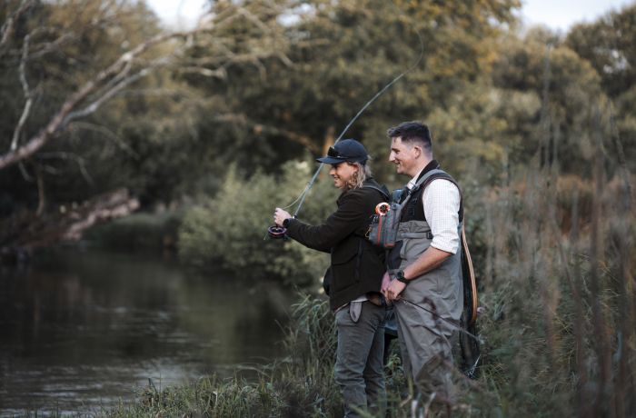man learning to fly fish with guide by side of river