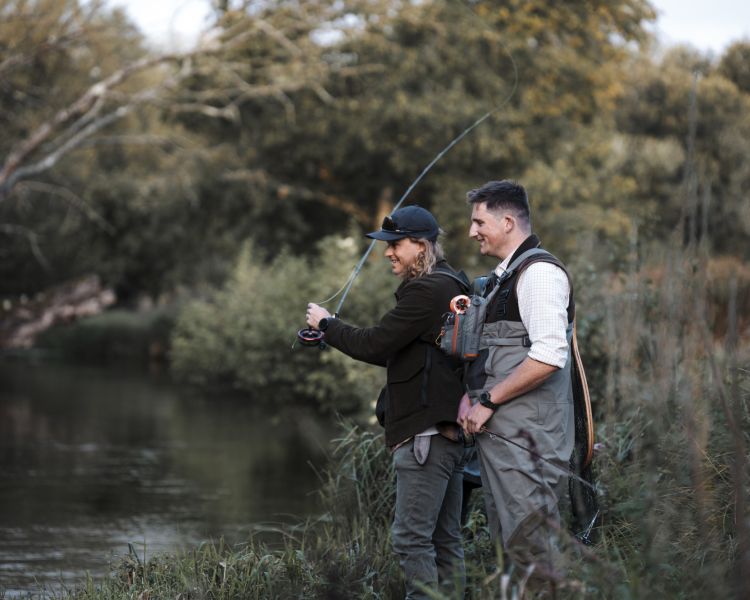 man learning to fly fish with guide by side of river