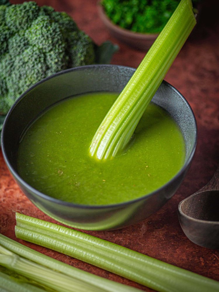 bowl of celery soup with broccoli and celery next to it