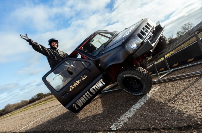 man hanging out of drivers door of stunt car up on two wheels