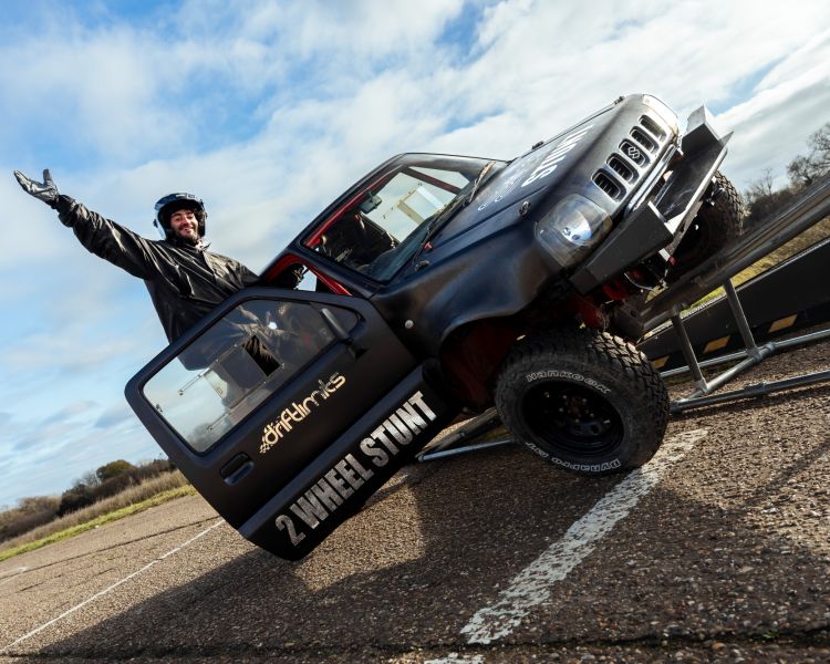 man hanging out of drivers door of stunt car up on two wheels