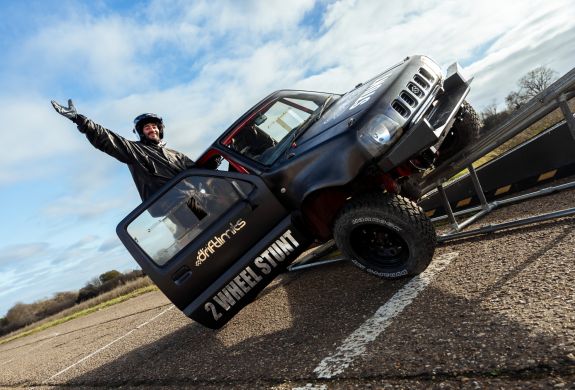 man hanging out of drivers door of stunt car up on two wheels