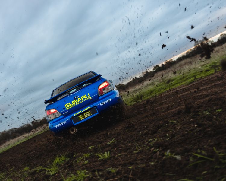 rear view of a subaru impreza on a dirt track with mud flying on a rally driving experience day
