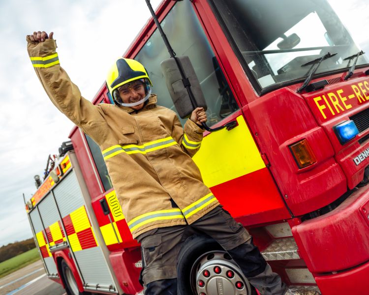 boy dressed as fireman next to fire engine on a fire fighting experience