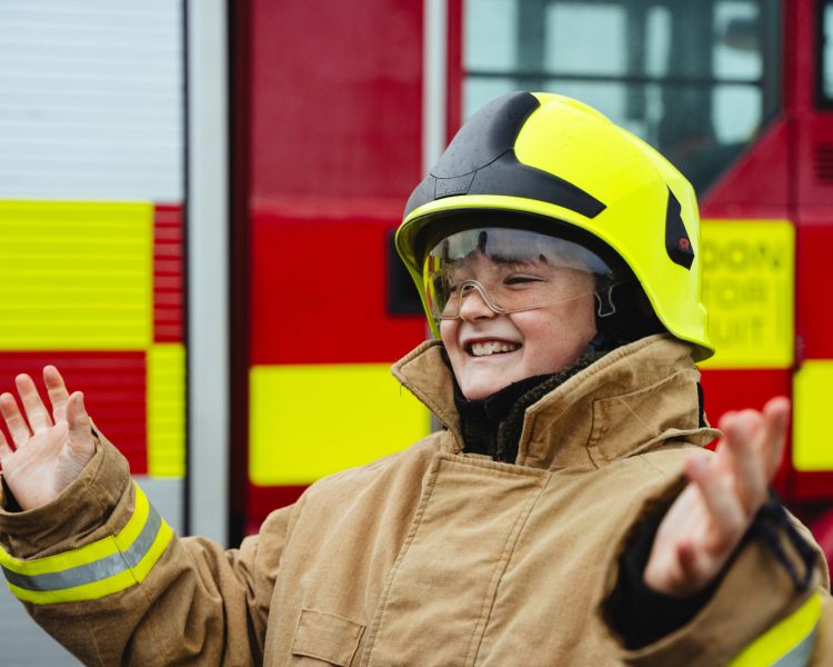 boy dressed as fireman next to fire engine on a fire fighting experience