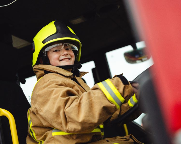 boy dressed as fireman sitting in fire engine on a fire fighting experience