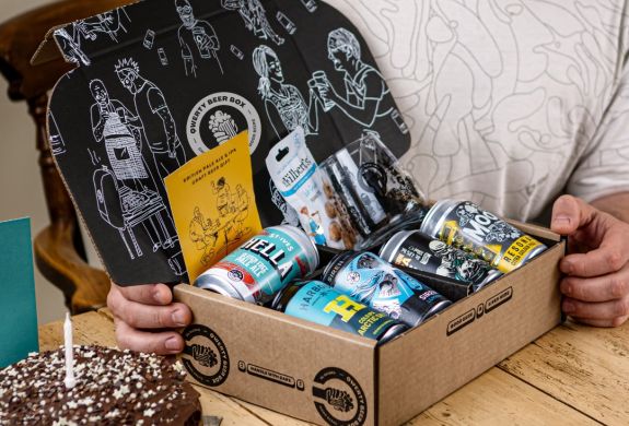 Man opening qwerty gift box of five cans of pale ale with snacks on birthday