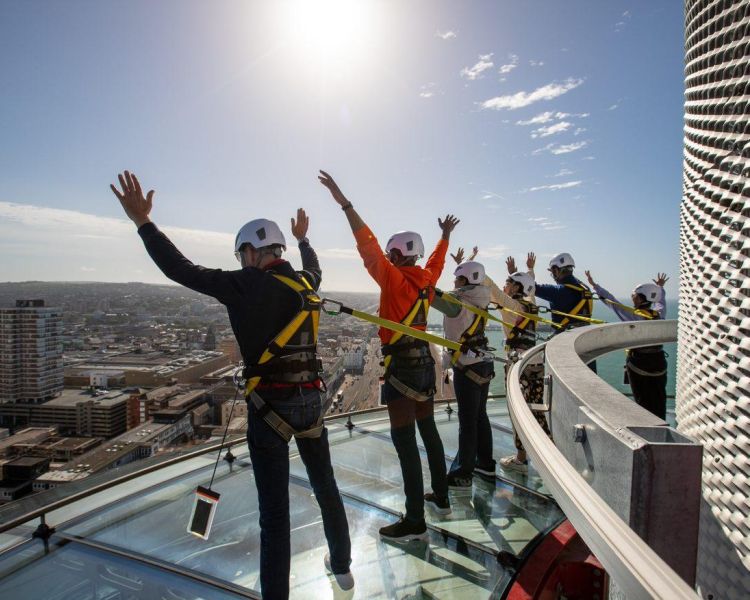people on the i360 sky walk with their hands in the air looking out at view